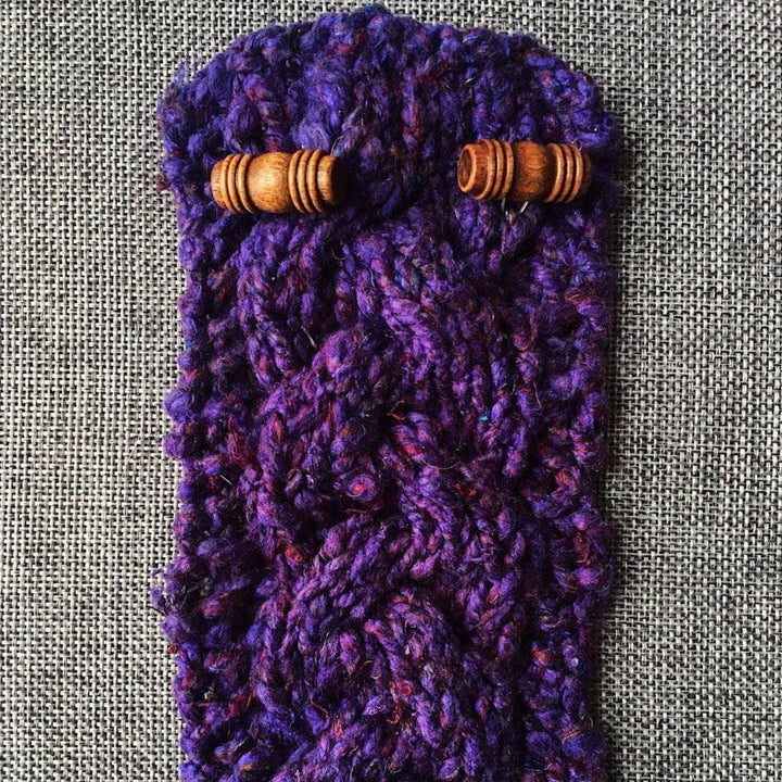 Purple knitted cozy with wooden buttons sitting on a gray fabric surface
