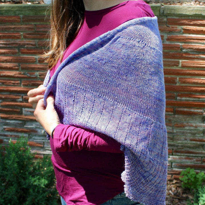 Woman standing in front of a brick wall wearing a Calico Scallop Shawl in purple