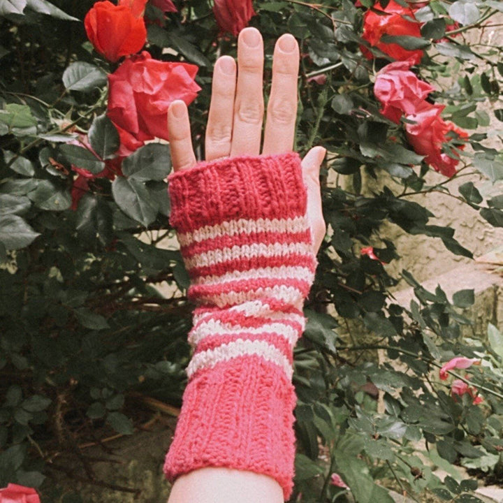 person wearing a pink and white stripped glove outside with roses in the background