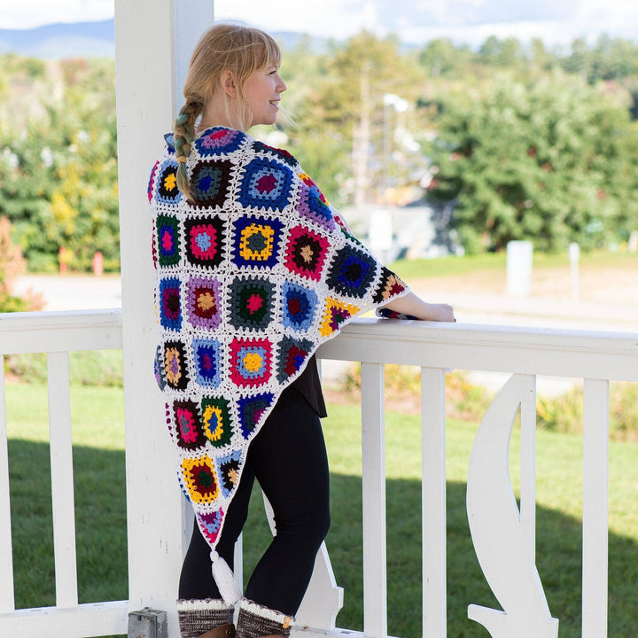 Model wearing cape cod granny square shawl with hands on a white railing, looking out over a mountainous landscape.