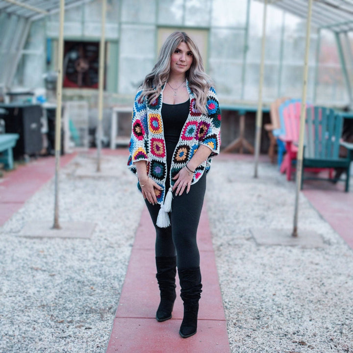 Model is standing in a greenhouse wearing Cape Cod Granny Square Shawl.