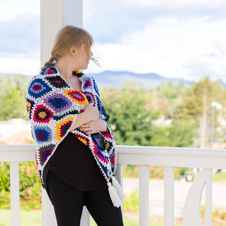 model wrapped in colorful granny square shawl looking out over a mountain vista.
