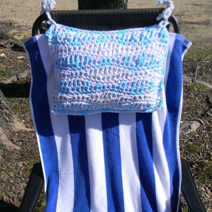 Blue and lavender crocheted Cast Away pillow tied to a black outdoor chair with a blue and white striped beach towel