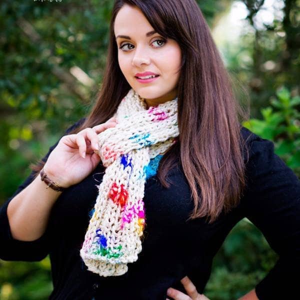 Woman in the woods wearing a multicolored knit Celebration scarf