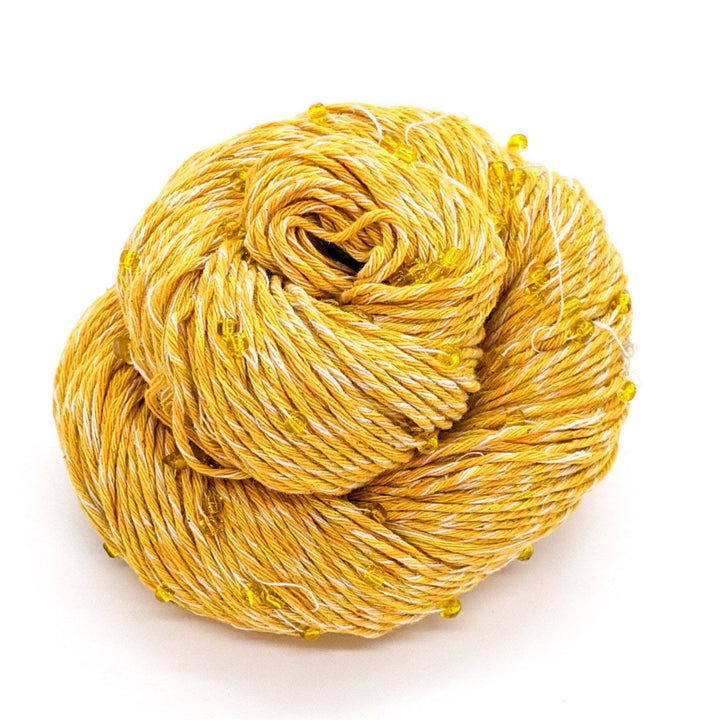 Chakra beaded cotton yarn in confidence. Yellow and white yarn with yellow beads and crystals throughout, sitting in front of a white background. 