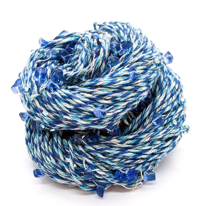 Chakra beaded yarn in expression infront of a white background. Blue and white yarn with blue beads and crystals throughout.