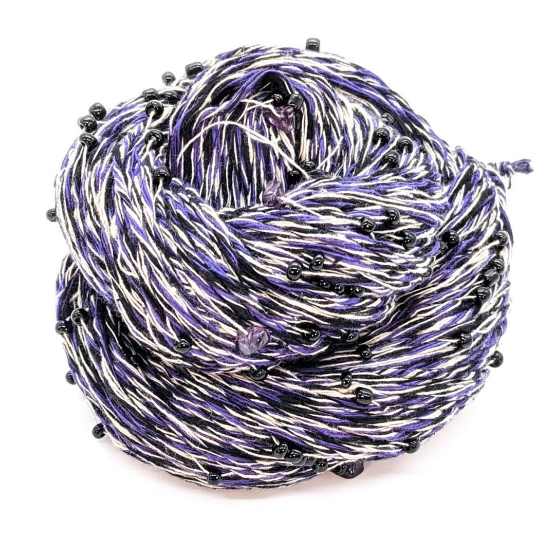 Chakra beaded yarn in intuition in front of a white background. Purple white and dark purple yarn with purple beads and crystals throughout. 