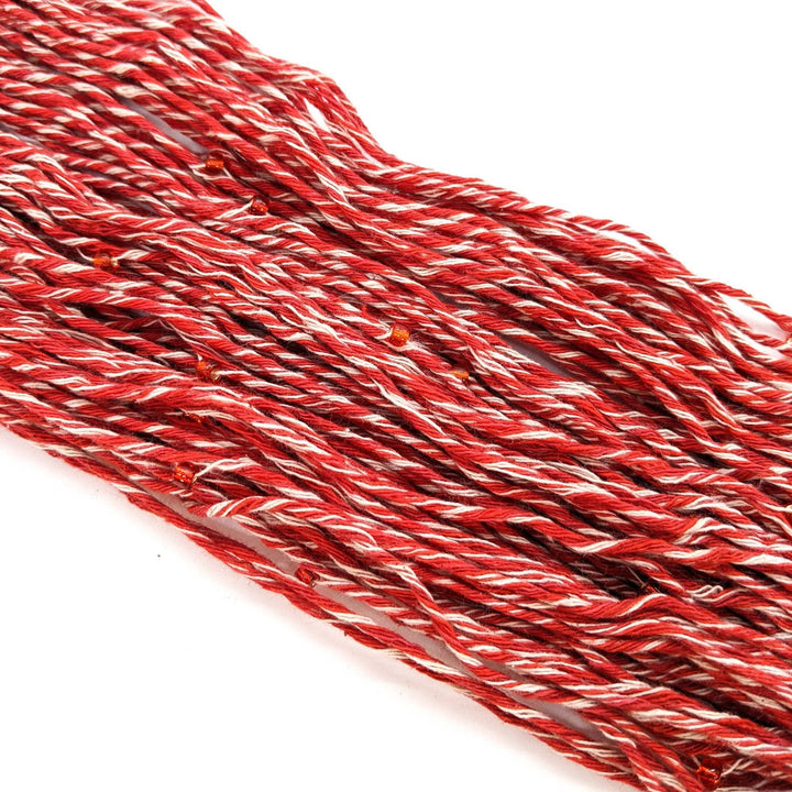 Chakra beaded cotton yarn in stability unskeined. Red and white marled yarn with red beads throughout, in front of a white background. 