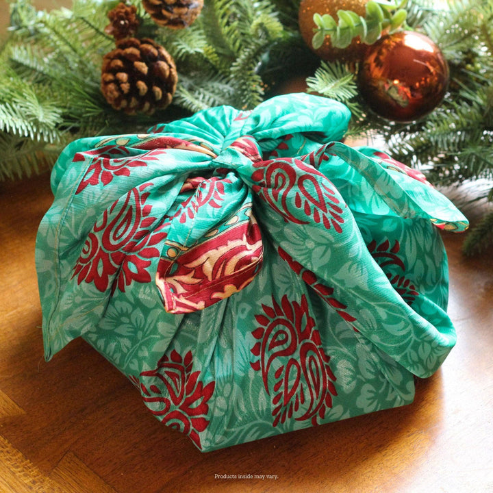 A christmas present idea sitting in front of holiday garland. The present is wrapped in green reusable gift wrapping made from reclaimed sari.