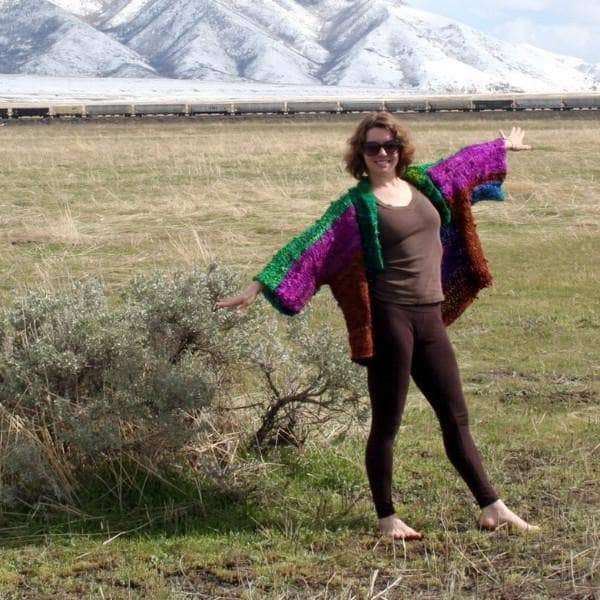 Woman wearing an oversized wide sleeve multicolor knitted jacket and standing in a grassy field
