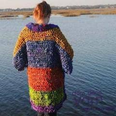 Back view of a woman wearing an oversized wide sleeve multicolor knitted jacket and standing in front of a lake