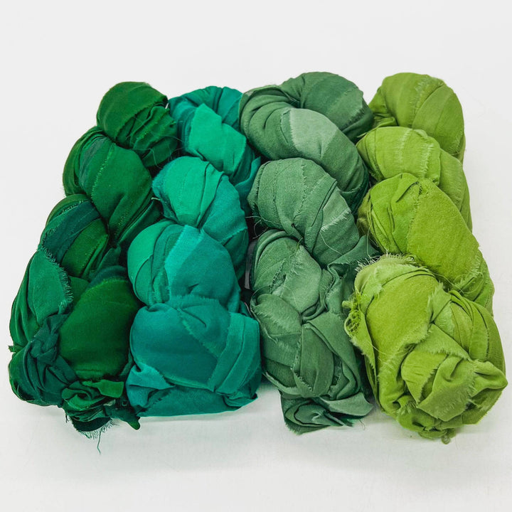 Jungle chiffon ribbon yarn ombre pack in front of a white background. Left to right: Emerald green, sea foam green, dark sage green, lime green.