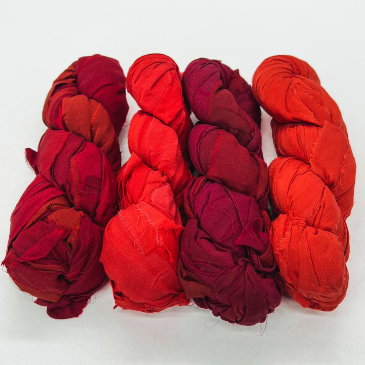 Lava chiffon ribbon yarn ombre pack in front of a white background. Left to right: Deep red, bright red, maroon, red-orange.