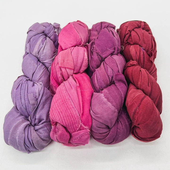 Lipstick chiffon ribbon yarn ombre pack in front of a white background. Left to right: lilac, vibrant pink, mauve, blood orange.