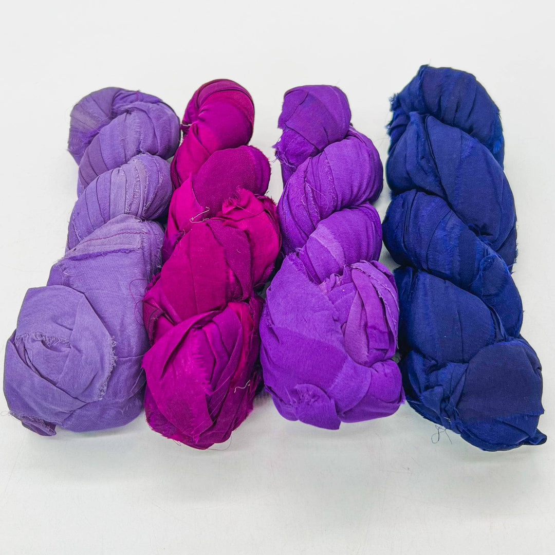 Mumbai chiffon ribbon yarn ombre pack in front of a white background. Left to right: lilac, magenta, lavender, royal purple.