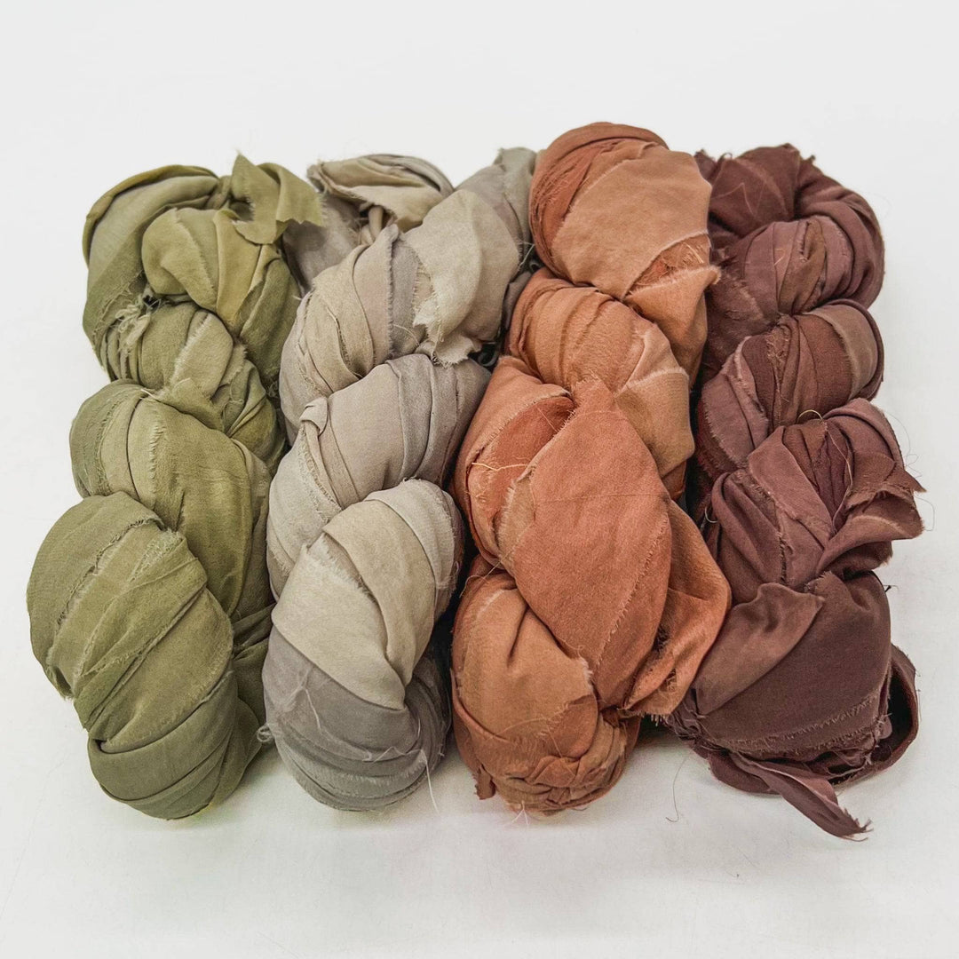 Neutrals chiffon ribbon yarn ombre pack in front of a white background. Left to right: Sage green, taupe, sandstone, brown.
