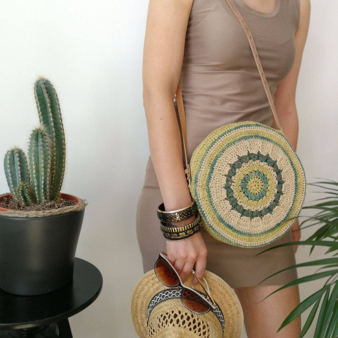 Woman wearing beige dress, circle banjo bag, straw fedora, and standing against a white wall with cactus plant