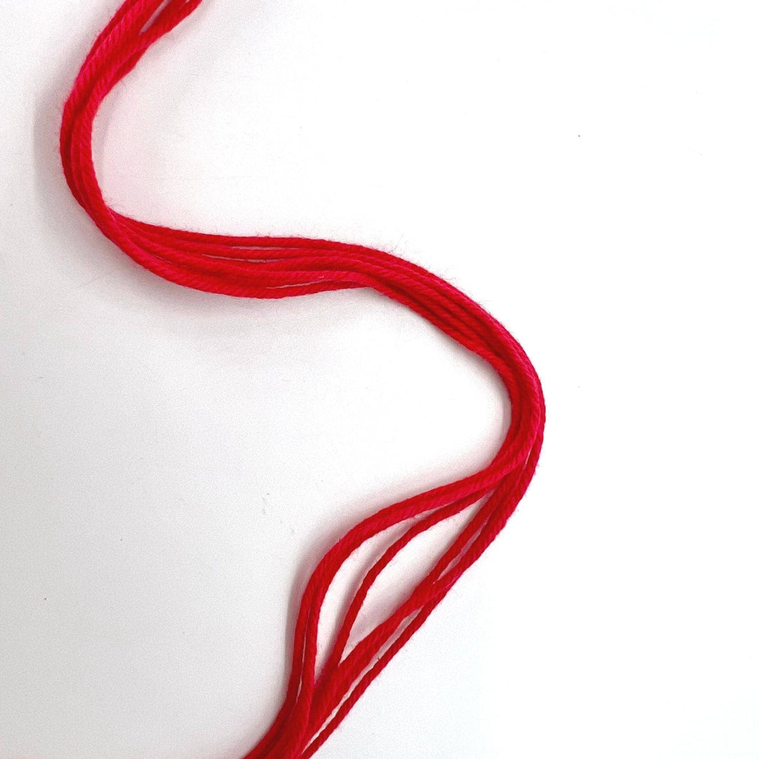 strands of raspberry red cotton yarn in front of a white background.