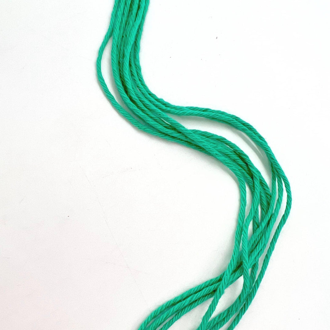 7 strands of teal cotton yarn in front of a white background.