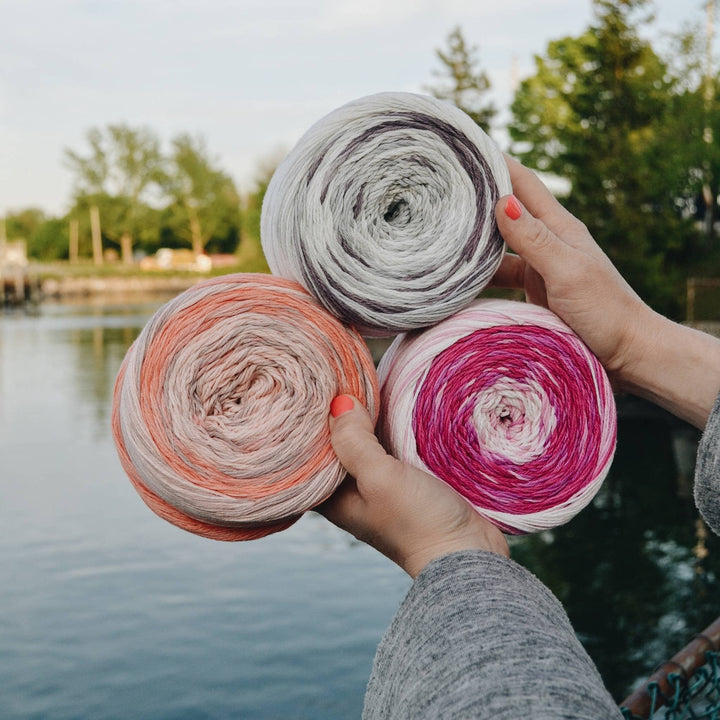 3 skeins of circulo whoopee being held up with lake and greenery in the background.