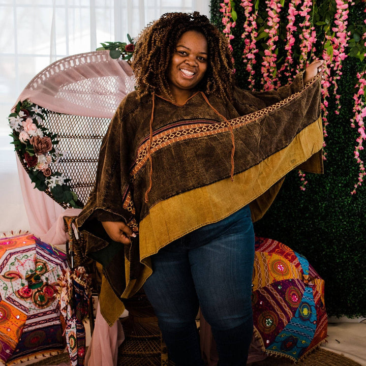 Model wearing green claire hooded poncho in front of a colorful background. Poncho is solid green with strip of lighter green fabric at the hem and horizontal strip of woven detailing on front panel.