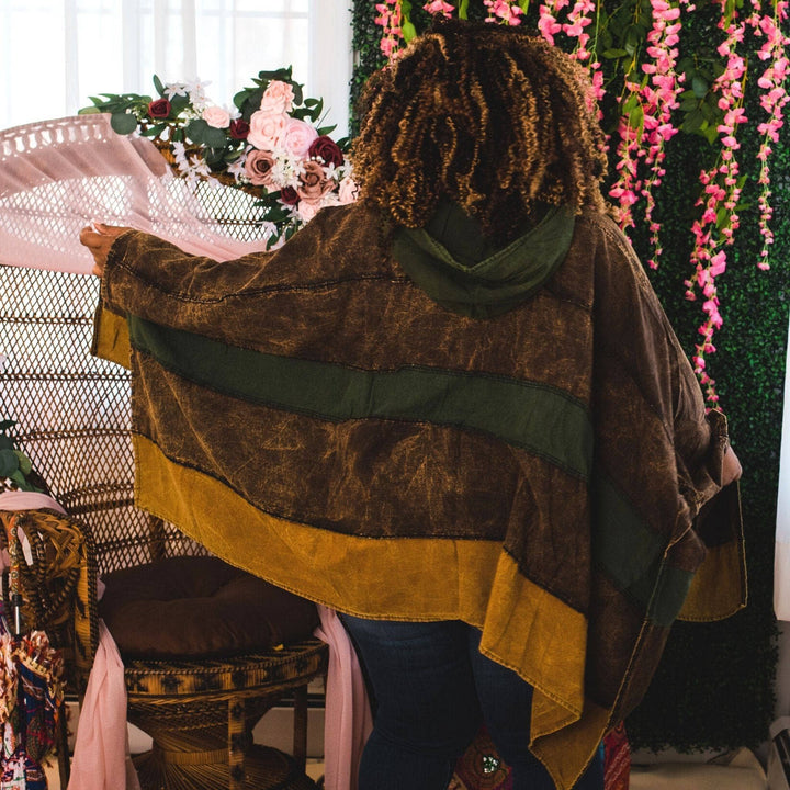 Back view of model wearing green claire hooded poncho in front of a colorful background.