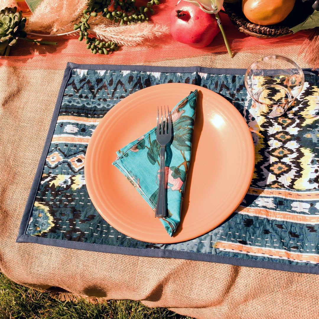 A blue cloth napkin folded into a triangle on a plate with a fork on top. 