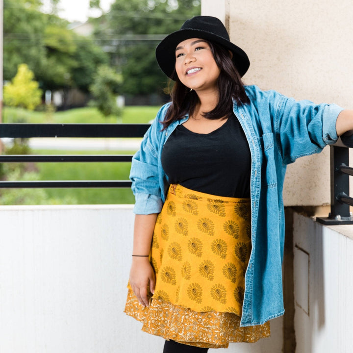 model wearing mini yellow sari wrap skirt in front of black and white all with greenery out the window.