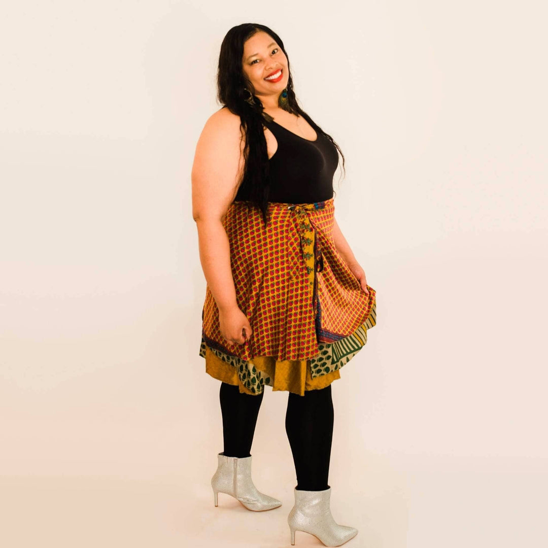 Smiling woman in black top and colorful patterned skirt. Long dark hair, silver boots.
