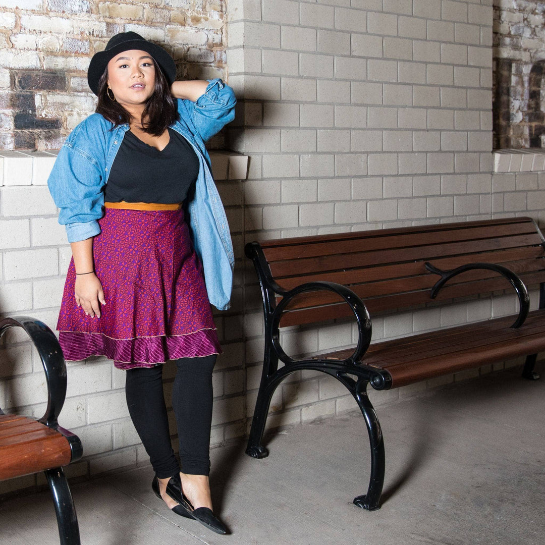 A woman in a purple wrap skirt and denim jacket posing beside a bench.