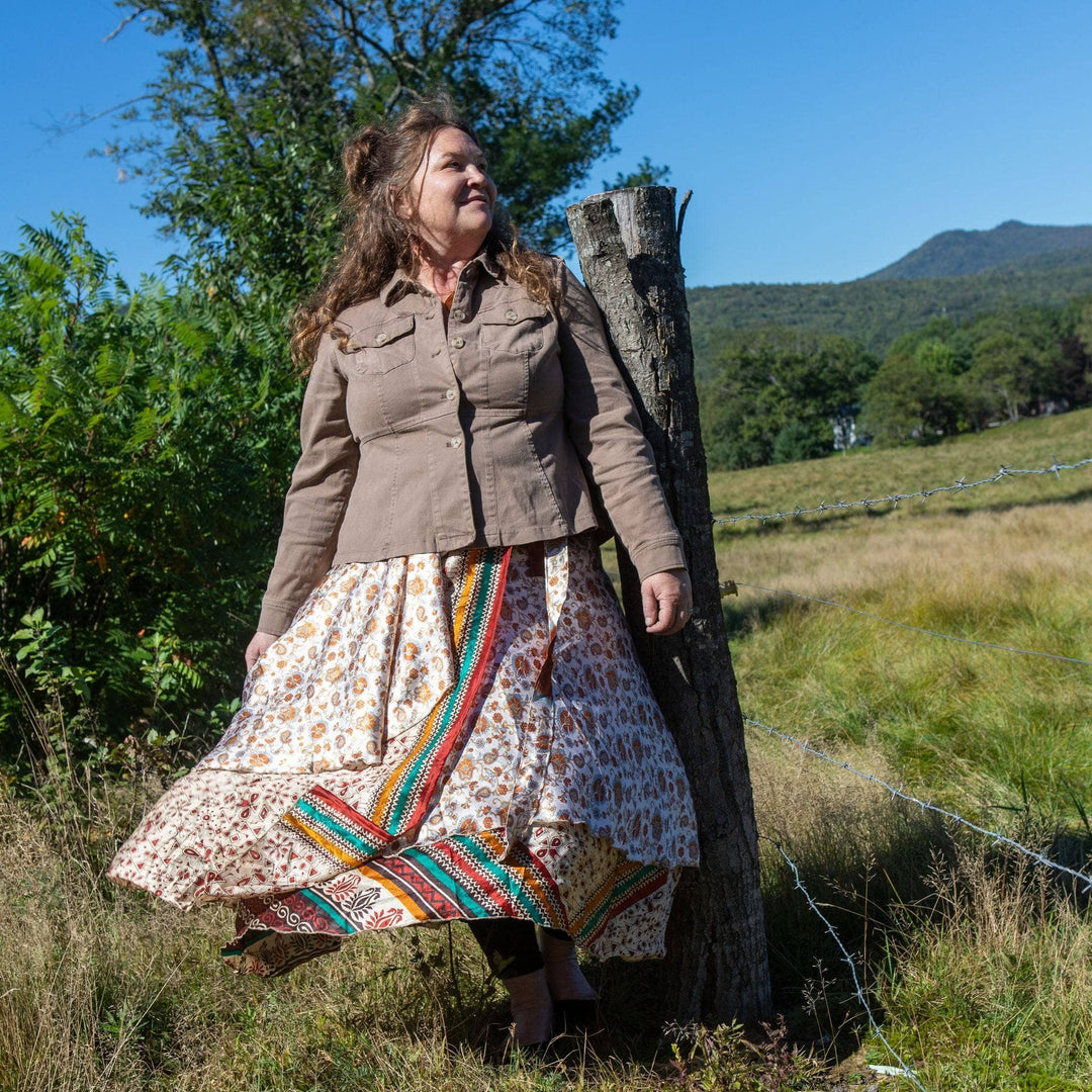 A woman in a printed wrap skirt posing outdoors by a wooden post.