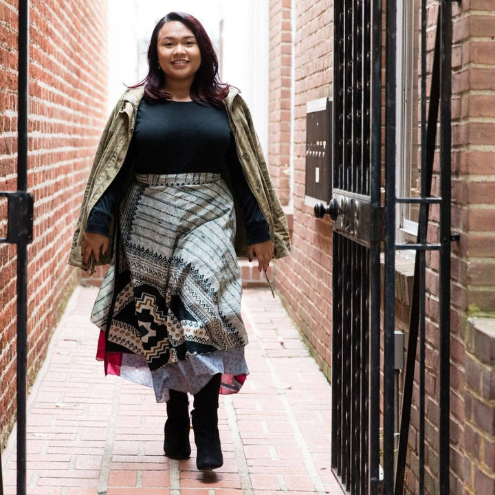 A woman walking in a narrow alleyway, wearing a patterned wrap skirt and a jacket.