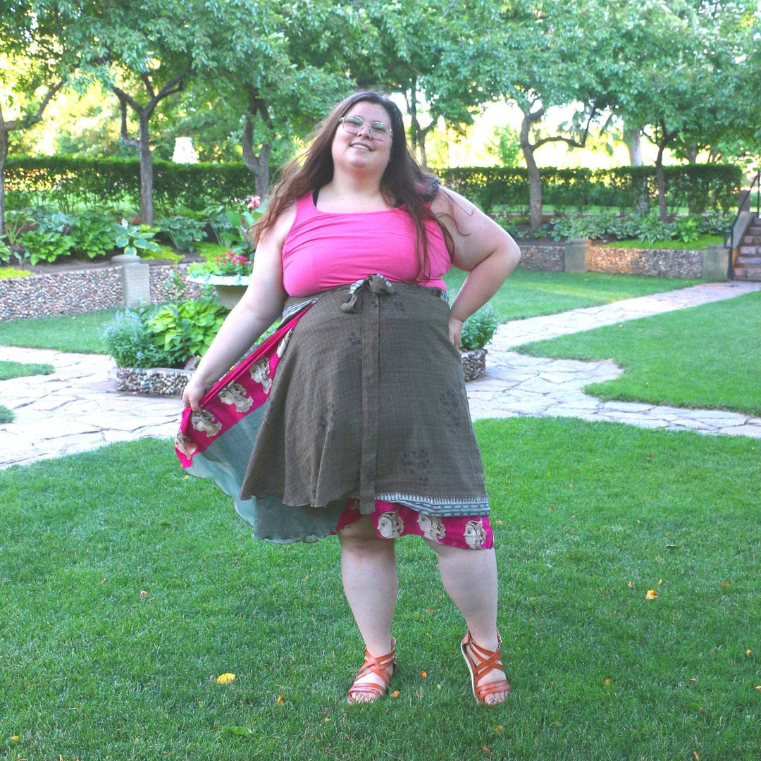  Woman in a park wearing a layered wrap skirt and pink top, posing cheerfully.