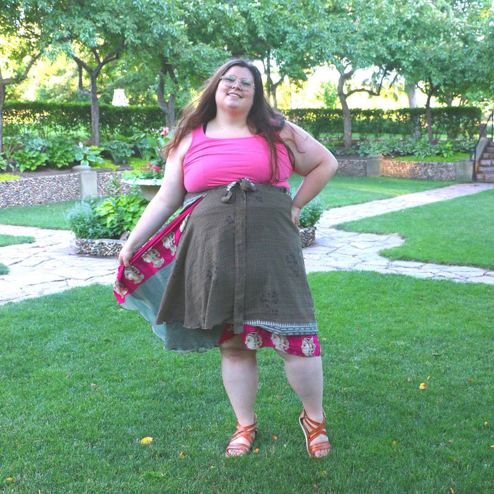  Woman in a park wearing a layered wrap skirt and pink top, posing cheerfully.