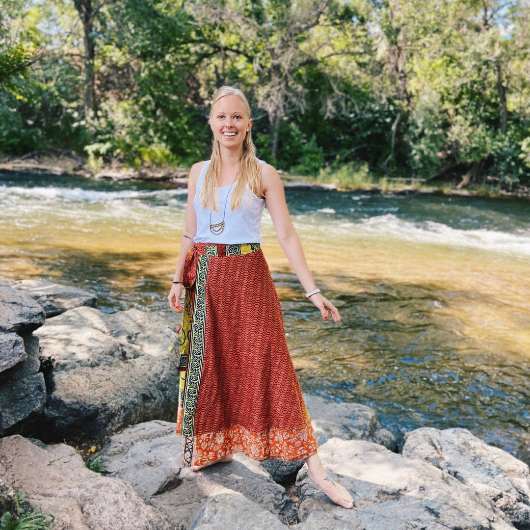 Woman in a red patterned wrap skirt by a river, smiling and enjoying nature.
