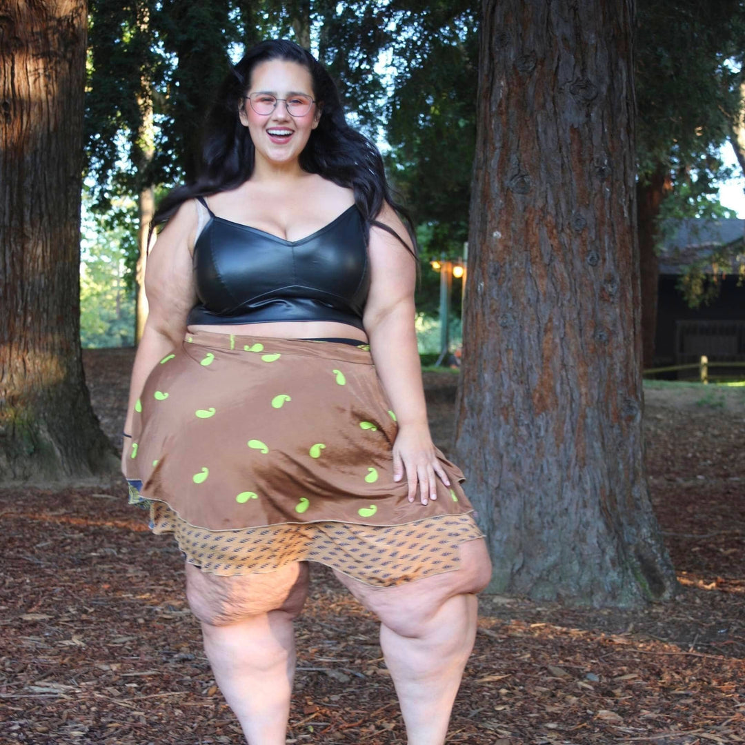 Woman in a park wearing a black top and brown skirt, smiling brightly.