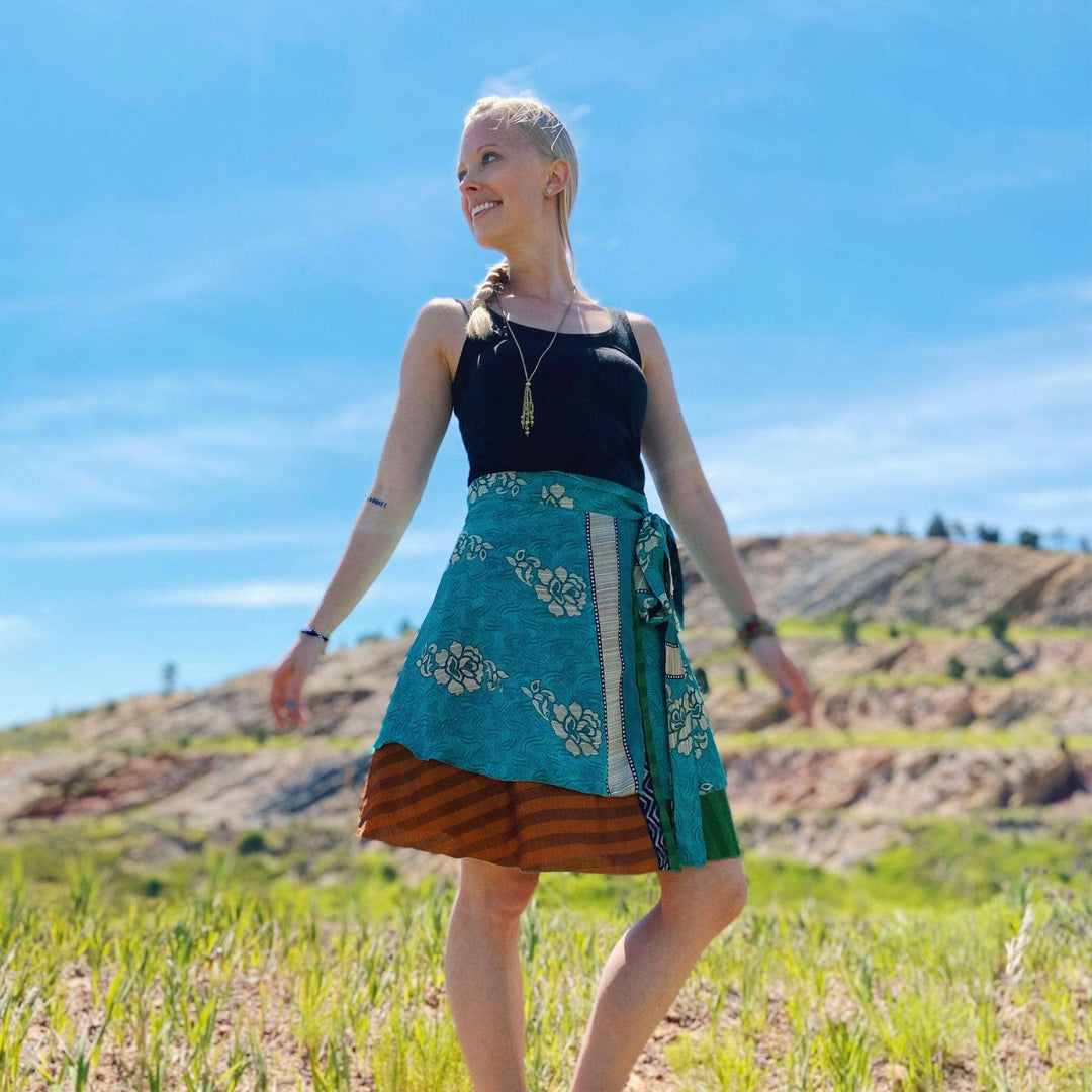 A woman in a teal and brown wrap skirt posing outdoors against a blue sky.