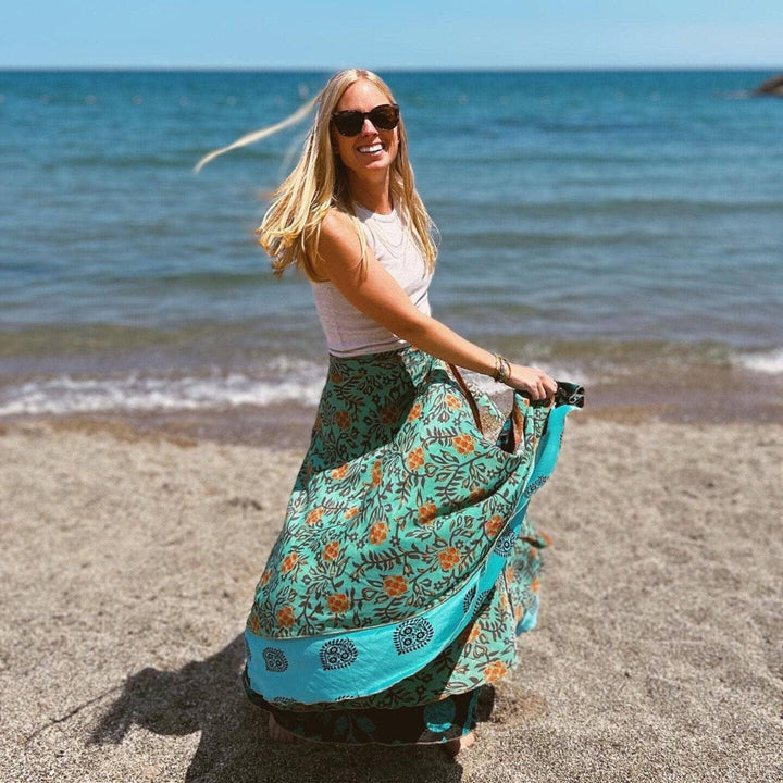 Woman twirling in a skirt on a beach, smiling and enjoying the sun.