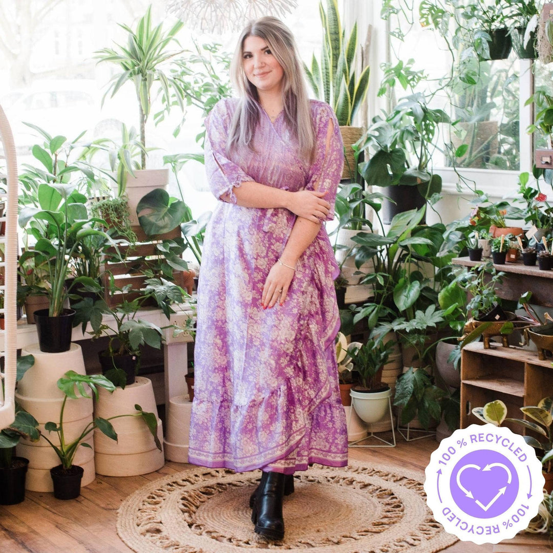 A blonde woman shopping in a floral shop in a floral baby pink wrap dress. Styled with tall black boots.