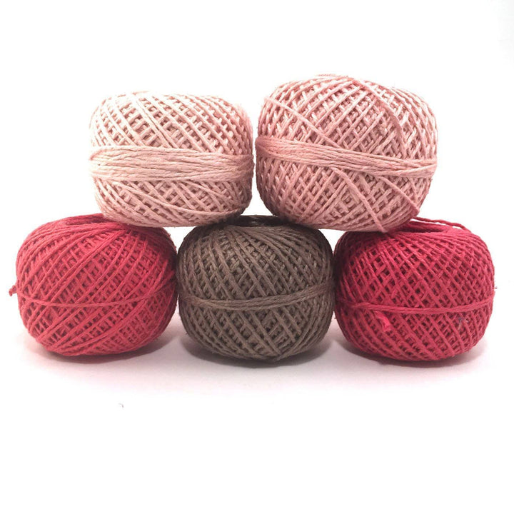 5 cakes of pink and brown yarns stacked on a white background