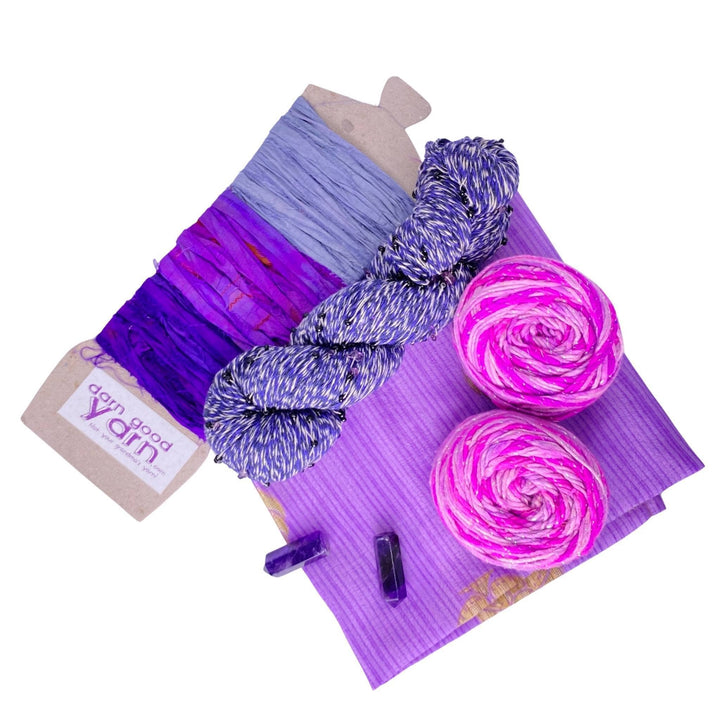 Amethyst energy bundle with all items showing in front of a white background. 2 amethyst, 2 skeins sparkle worsted weight silk, 1 skeins chakra beaded cotton yarn, 3 color sari silk ribbon sample card, and coordinating furoshiki.