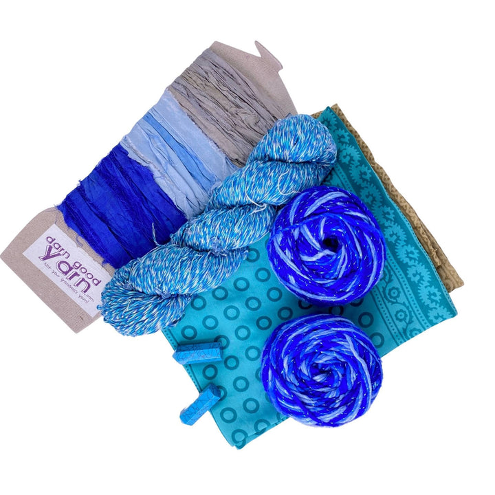 Lapis Lazuli energy bundle with all items showing in front of a white background. 2 lapis lazuli crystals, 2 skeins sparkle worsted weight silk, 1 skeins chakra beaded cotton yarn, 3 color sari silk ribbon sample card, and coordinating furoshiki.