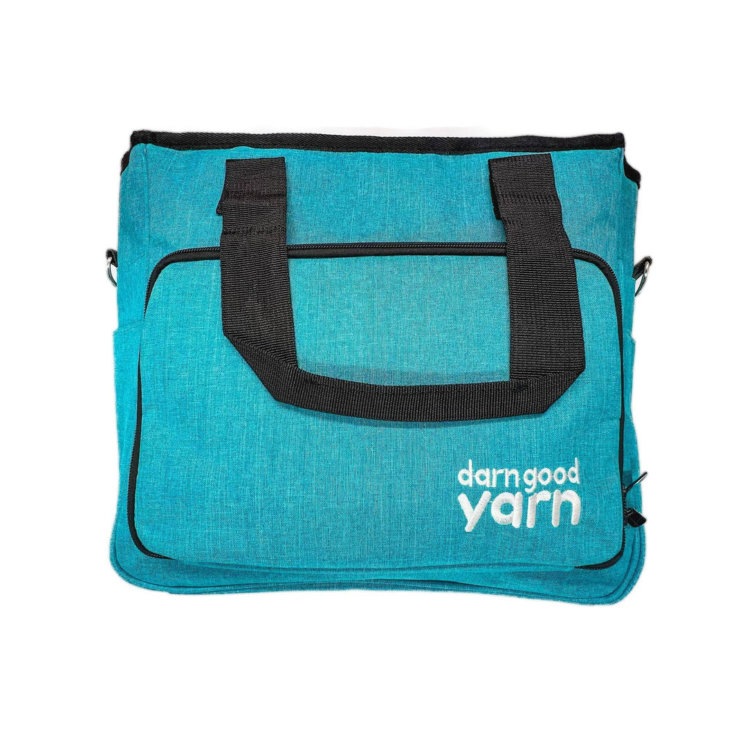 Darn Good Yarn crafters deluxe storage bag in front of a white background. Bag is teal with black zippers and handles, text on the bag reads Darn good yarn.