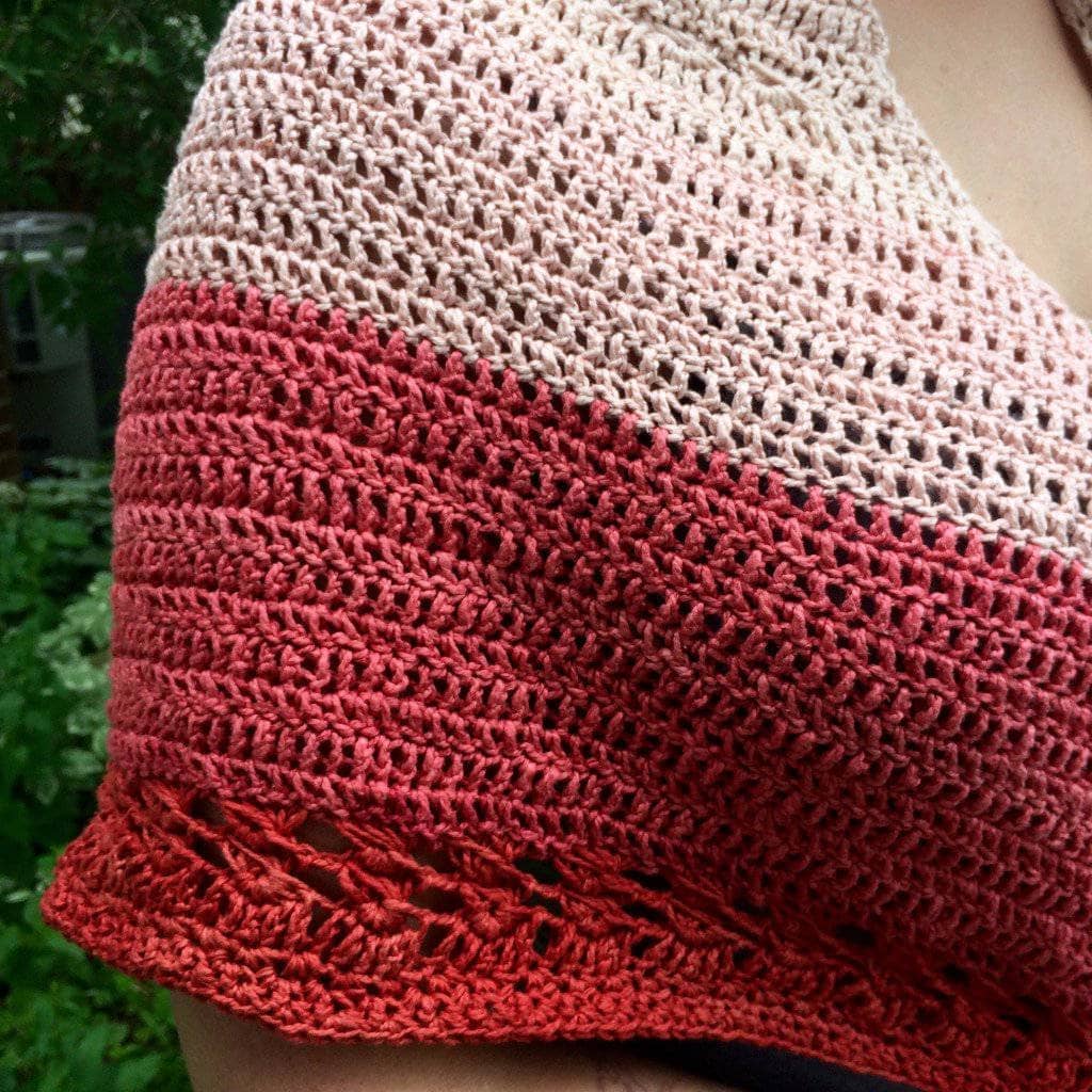 Close up image of a woman wearing a red and pink crochet shawl over one shoulder