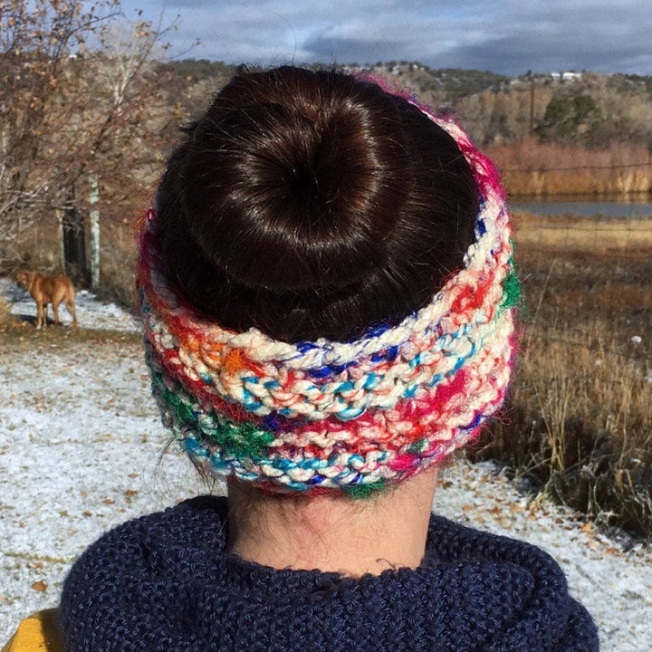 Back view of a woman's head wearing a multicolored knit headband standing in front of a snowy landscape