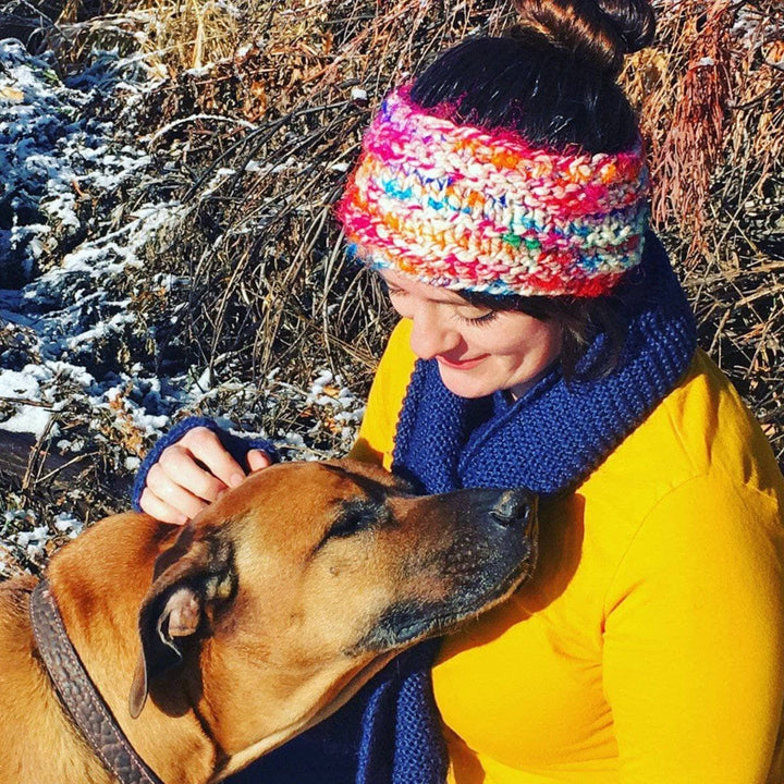 Woman in yellow sweater, blue scarf, and multicolored knit headband petting a dog