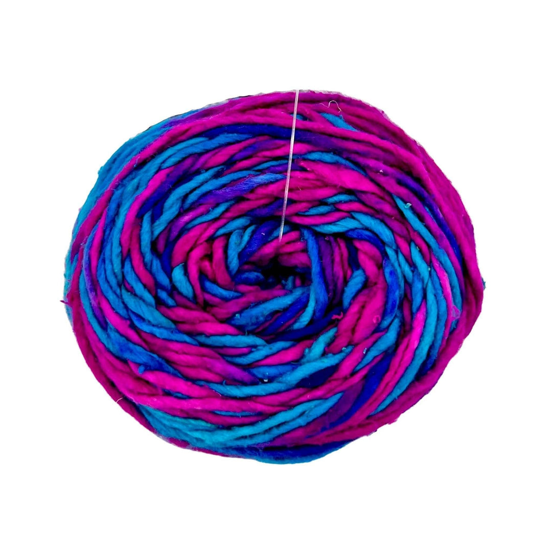 cake of silk roving worsted weight yarn in the colorway cupcake (variegated pink, blue, and purple) in front of a white background.