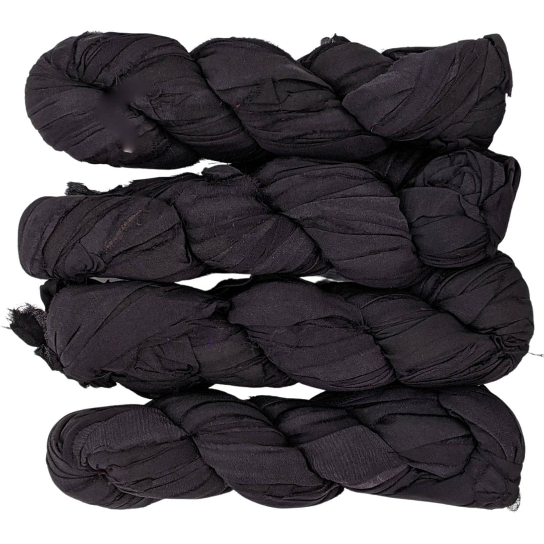 4 skeins reclaimed chiffon ribbon yarn all black in front of a white background.