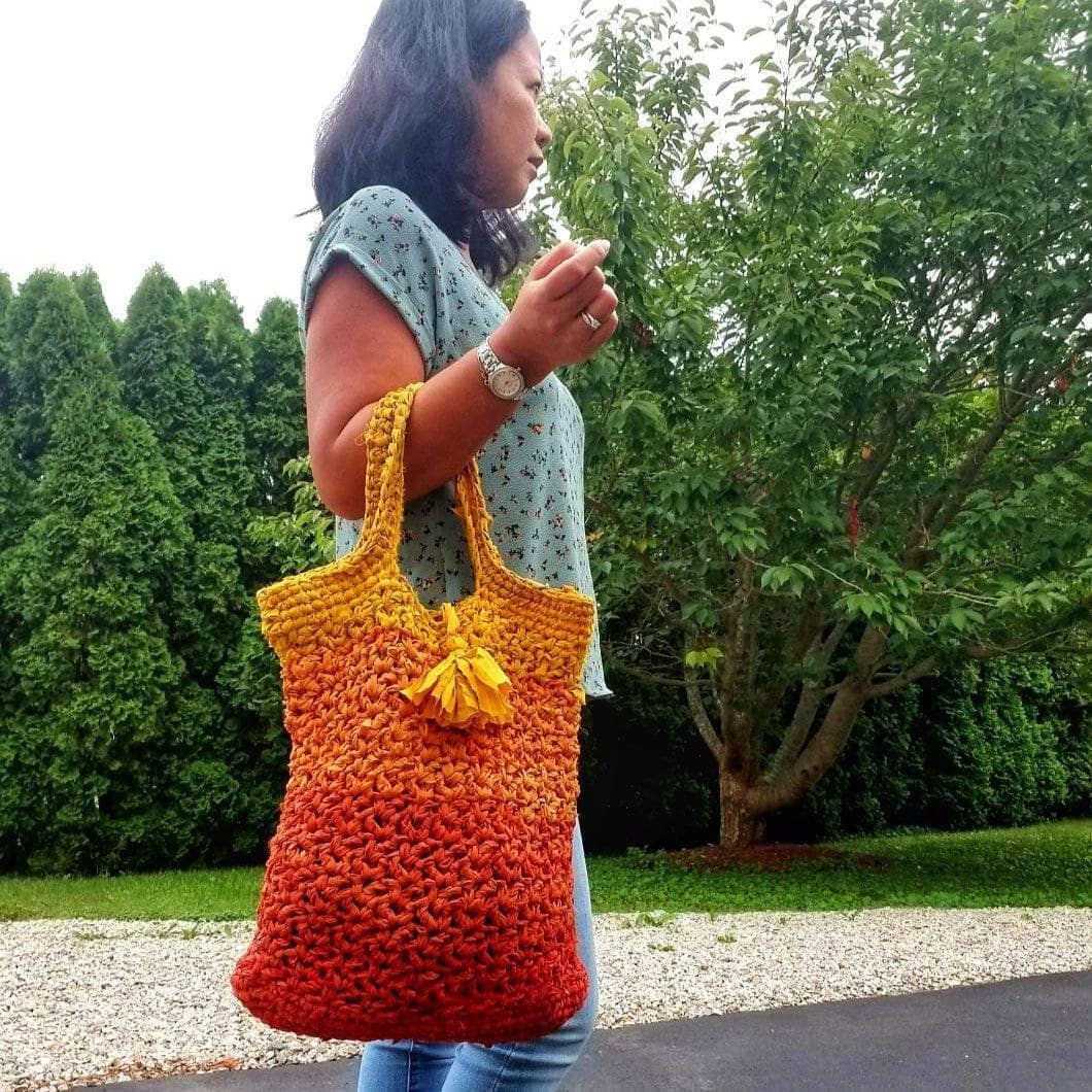 A woman holding a orange ombre tote bag outside 