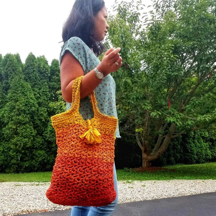 A woman holding a orange ombre tote bag outside 